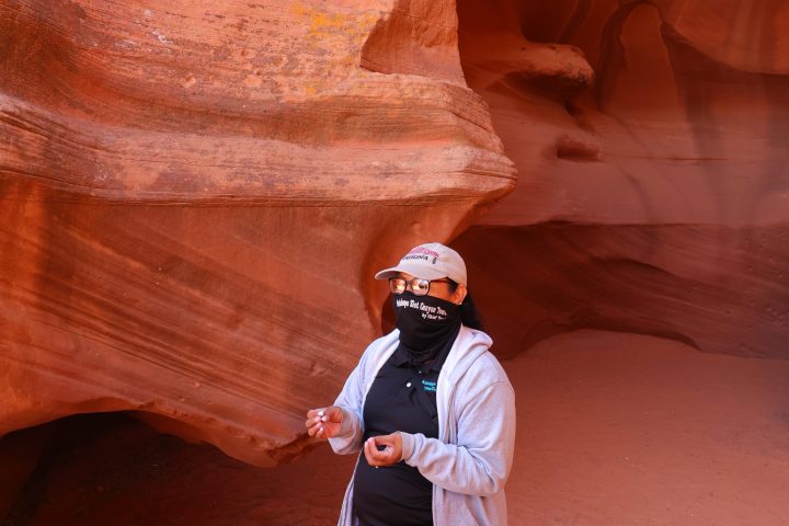 Person in canyon with red sandstone walls, wearing a cap and mask.