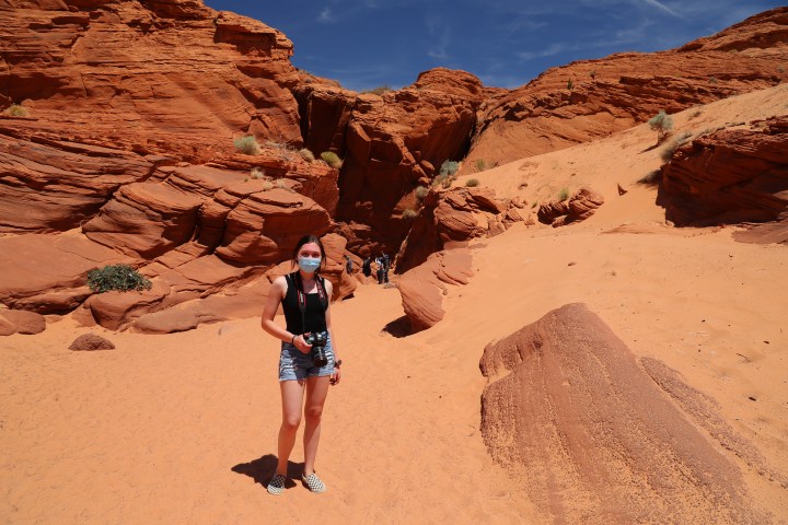 Person with camera in a red sandstone desert landscape, bright sky.
