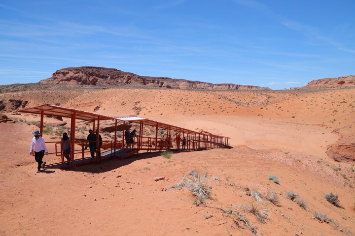 People walking on a covered pathway in a desert landscape.
