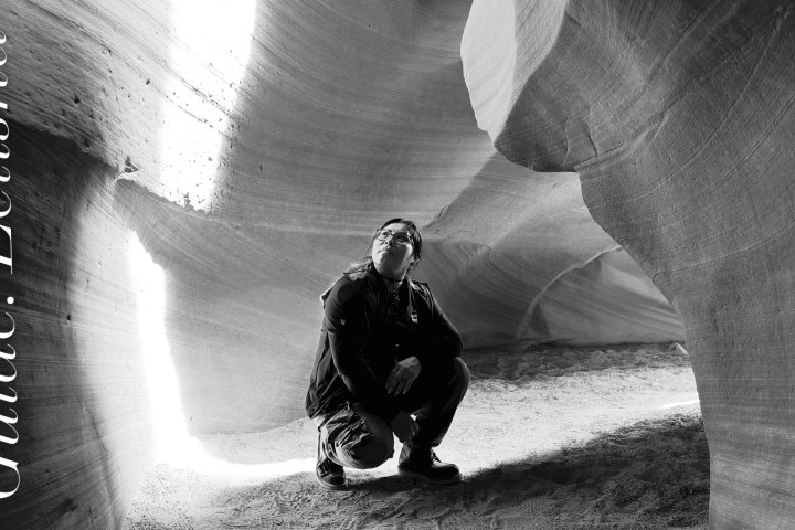 Person kneeling in a sunlit sandstone cave.
