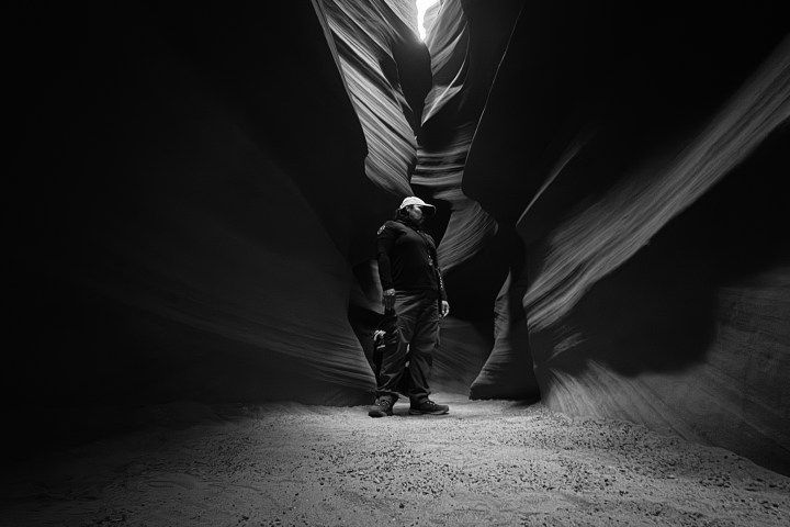 Person standing in a narrow, dark canyon with light from above.