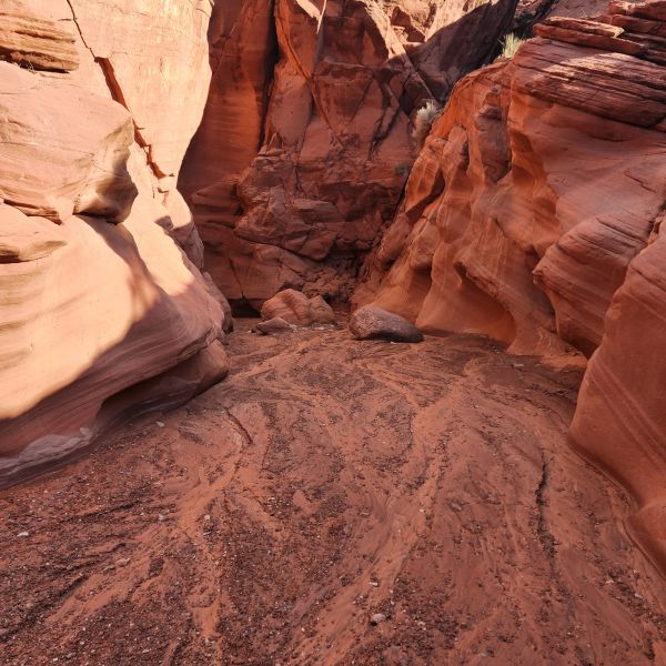 Narrow canyon with red rock walls and a rocky path under a clear blue sky.