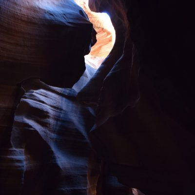 Sunlight beams highlight smooth, curved rock formations inside a dark cave.