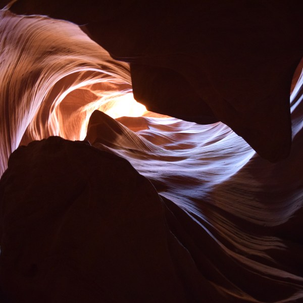 Sunlight illuminating swirling sandstone formations in a cave.